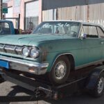 Teal car on tow truck, indicating potential for part salvage and sale.