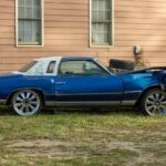 A heavily damaged car sits beside a house, waiting to be picked up for recycling, representing junk car removal services.