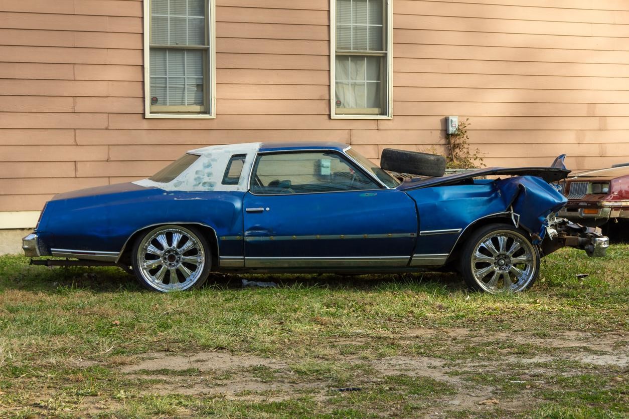 A heavily damaged car sits beside a house, waiting to be picked up for recycling, representing junk car removal services.