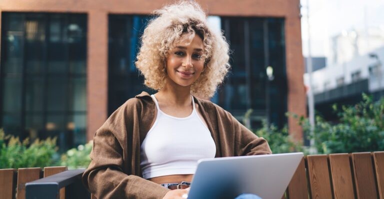 Young woman sitting on a bench with her laptop smiling researching the Spanish language levels